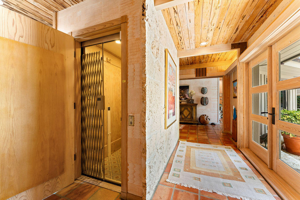 Wood-paneled hallway with terracotta tile, a gated elevator, and wood-framed glass doors.