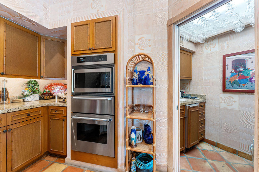 Kitchen with warm wood cabinets, a stainless double wall oven, patterned tile, and a rattan display shelf.