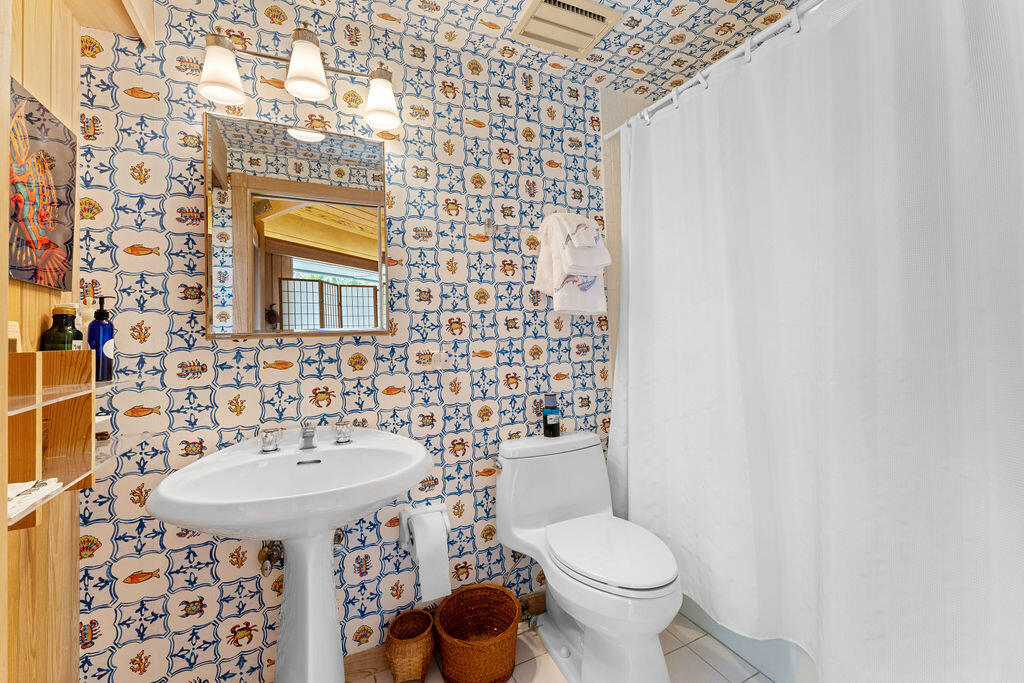 Bathroom with blue-and-orange patterned tile, a pedestal sink, toilet, and white shower curtain.