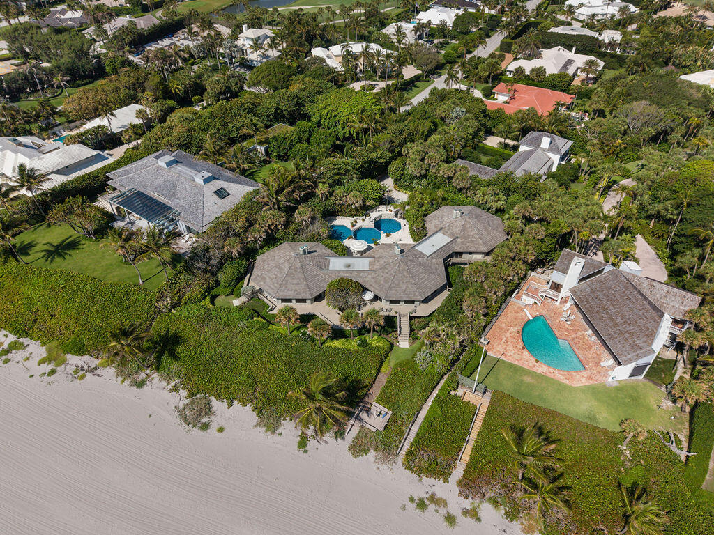 Beachfront home with a gray roof, tropical landscaping, and a pool beside the sandy beach.