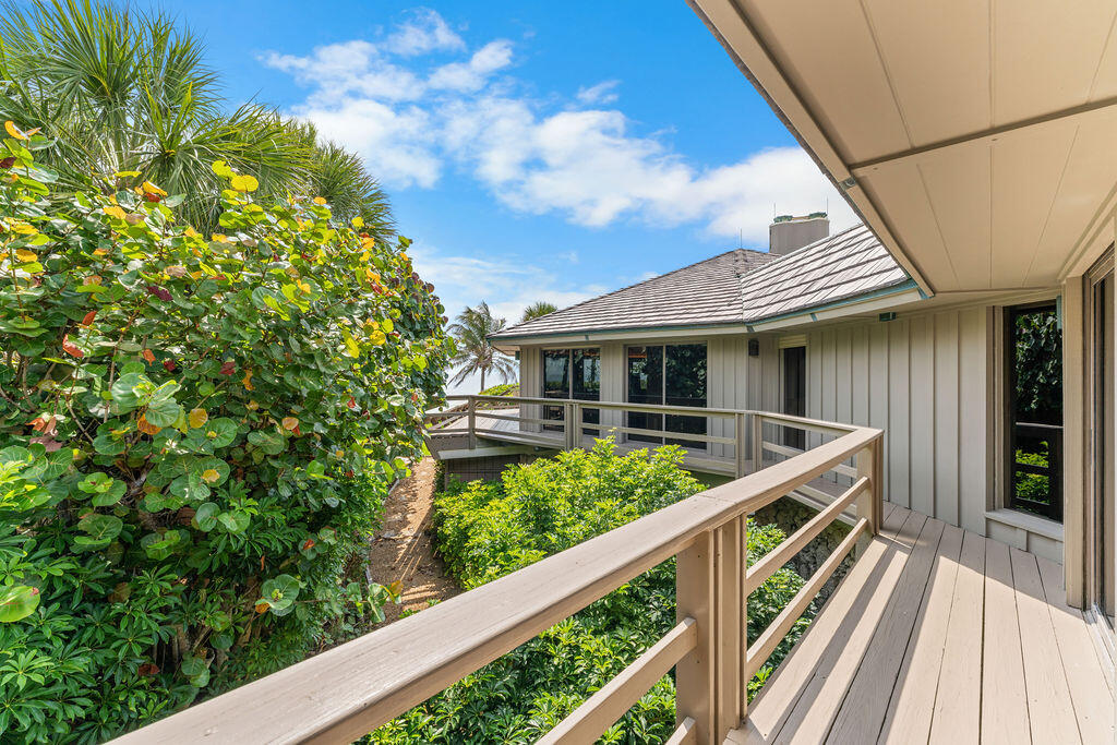 Exterior deck walkway beside lush tropical landscaping and a light-sided coastal home.