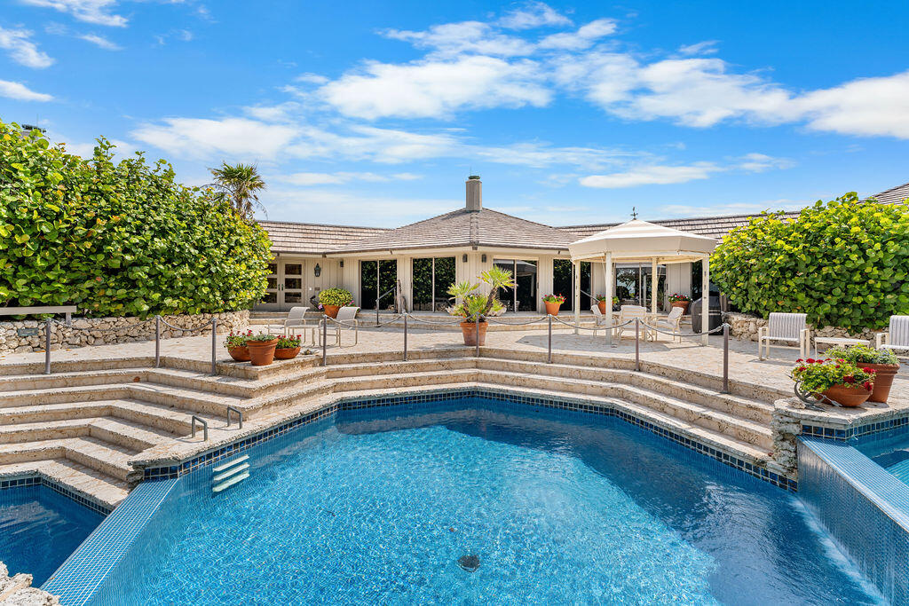 Backyard swimming pool with curved stone steps, potted flowers, and a covered patio.