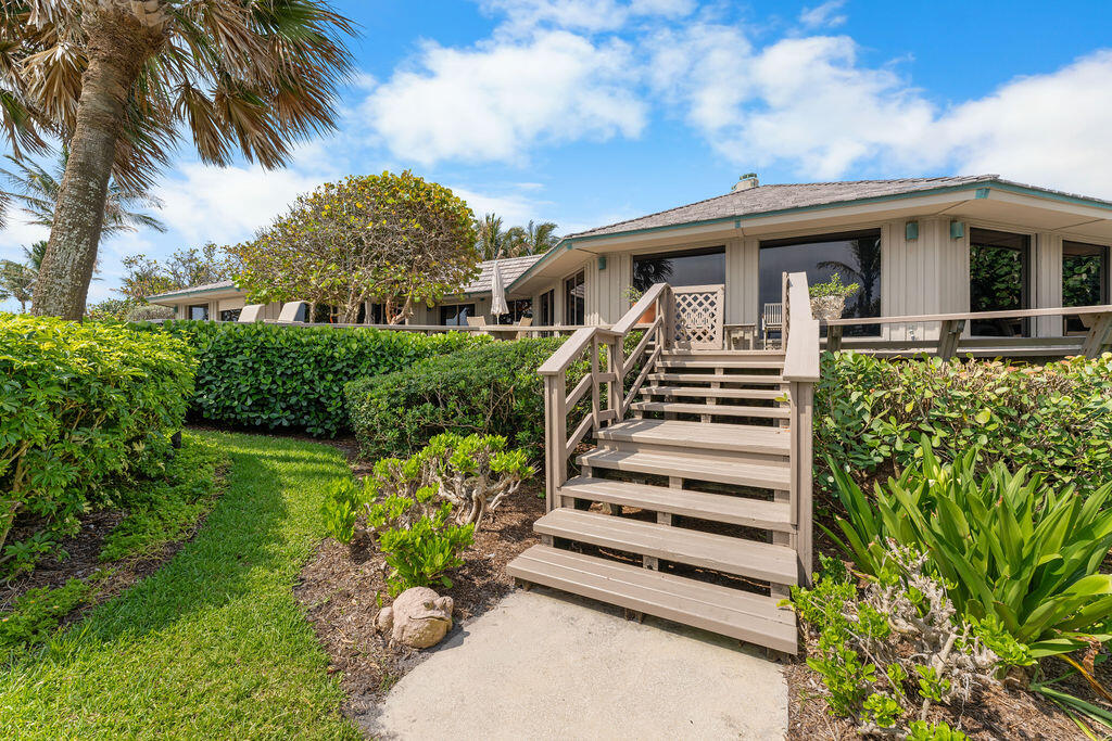 Single-story home with raised deck and central stairs, surrounded by tropical landscaping.