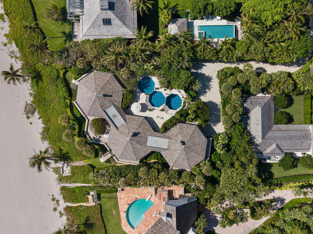 Aerial view of a beachfront estate with a large home, tropical landscaping, and several pools.