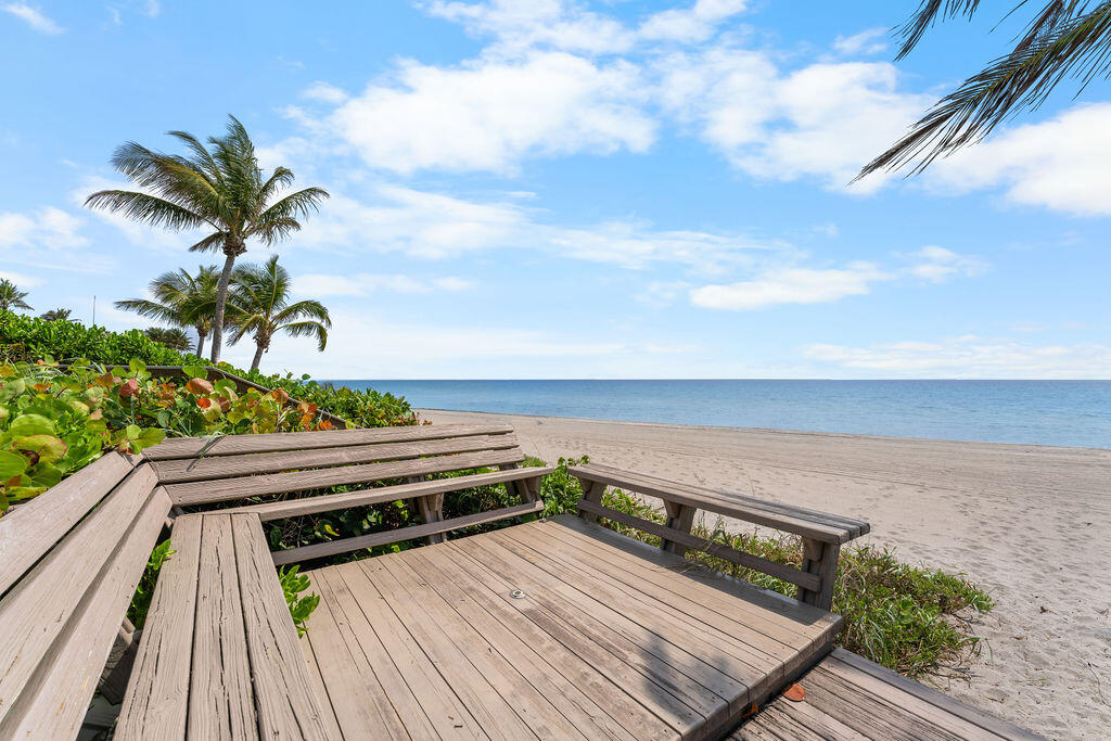Beachside deck with wooden benches overlooking a sandy beach and calm ocean.