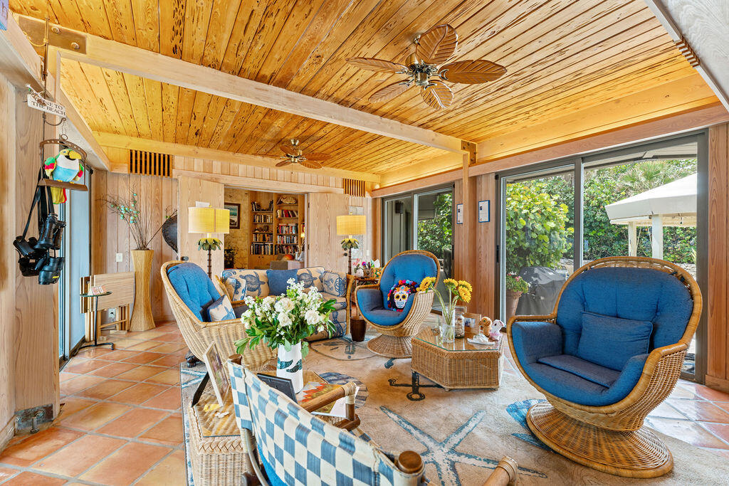 Living room with a vaulted wood ceiling, blue-cushioned wicker chairs, terracotta tile, and garden-facing glass doors.
