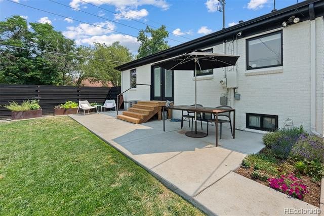 Backyard patio with an umbrella-covered dining table, wooden steps, lawn, and flower beds.