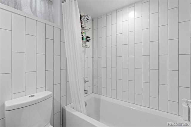 Bathroom with white tiled walls, a bathtub-shower, and a white curtain.