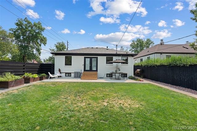 House backyard with a broad lawn, raised garden beds, black fencing, and a furnished patio.