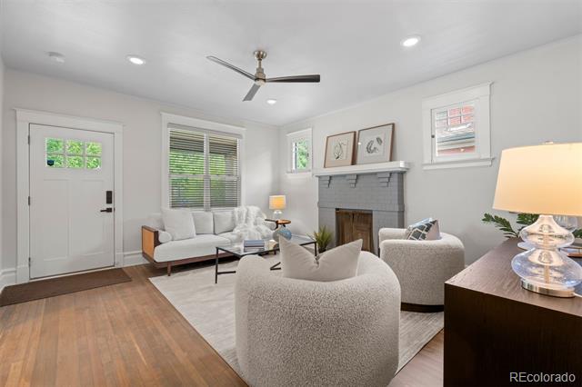 Living room with a gray fireplace, white seating, ceiling fan, and hardwood floors.