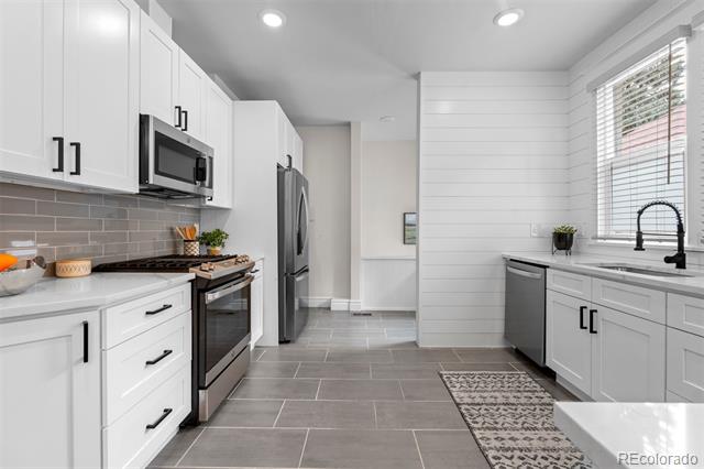Bright white kitchen with stainless steel appliances, gray tile floors, and a window above the sink.