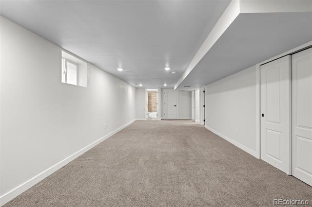 Vacant basement room with beige carpet, small high windows, and white closet doors.
