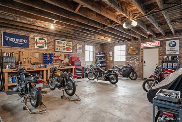 Motorcycle-filled garage with exposed timber rafters, brick walls, and workshop benches.