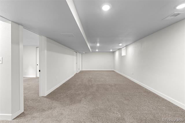 Finished basement with beige carpet, white walls, and recessed ceiling lights.