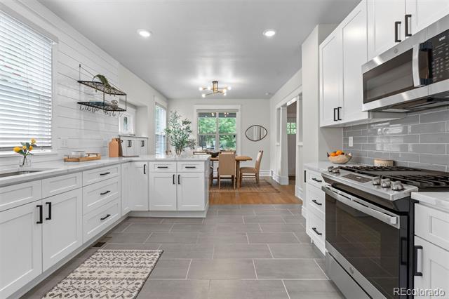Bright kitchen with white cabinets, gray tile floors, and stainless steel appliances.