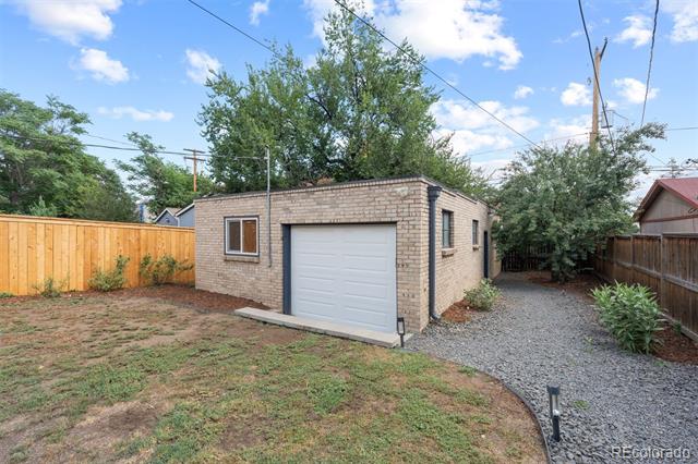 Detached brick garage with a white overhead door, gravel driveway, and fenced backyard.