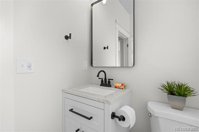 Modern bathroom with a white vanity, black fixtures, wall mirror, and potted plant on the toilet.