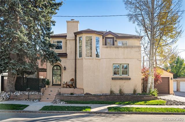 Two-story beige stucco home with an arched entry, front patio, and attached garage.