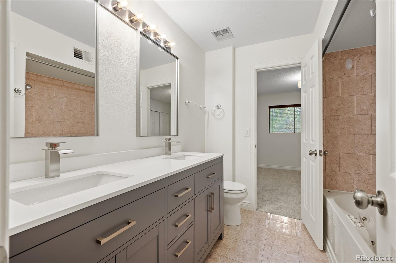 Bathroom with a double-sink vanity, large mirrors, and a tiled tub and shower.