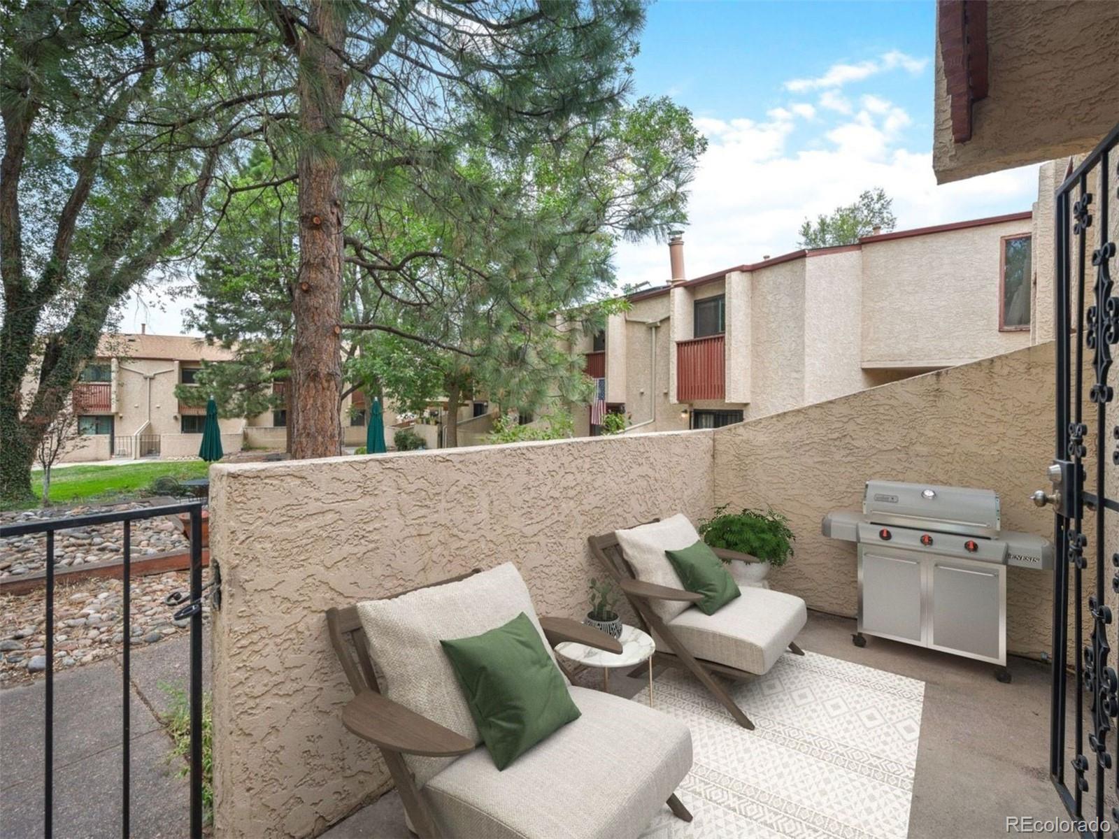 Private patio with cushioned lounge chairs and a stainless-steel grill beside a stucco wall.
