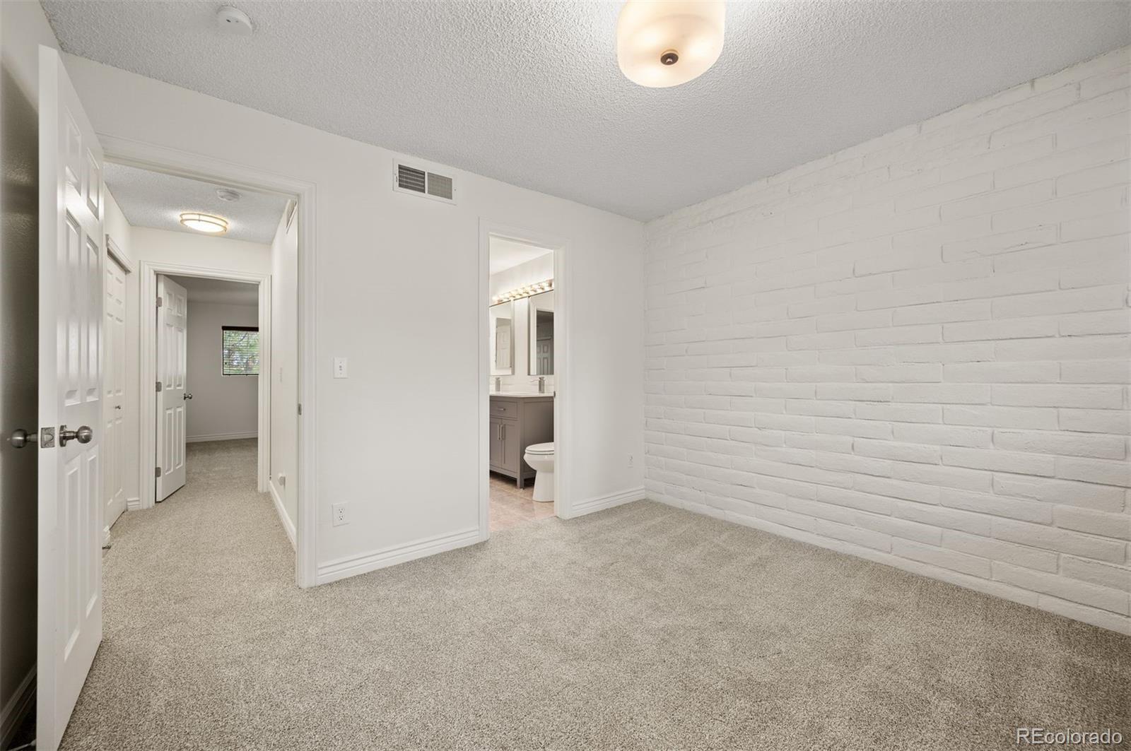 Unfurnished carpeted room with a white brick wall and an adjoining bathroom doorway.