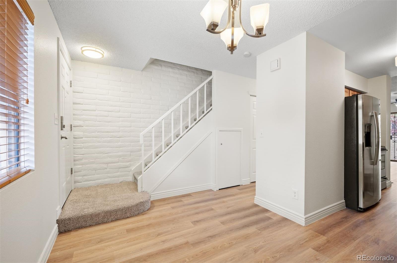 Entryway with a carpeted staircase, white brick wall, and stainless-steel refrigerator.