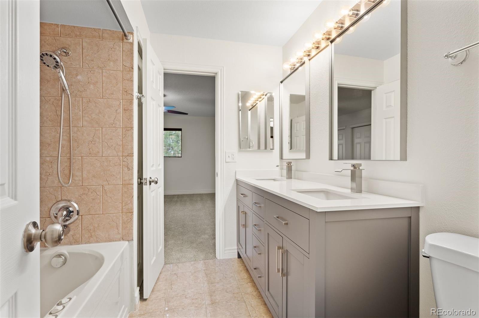 Bathroom with a gray double vanity and a tub-shower with tan tile.