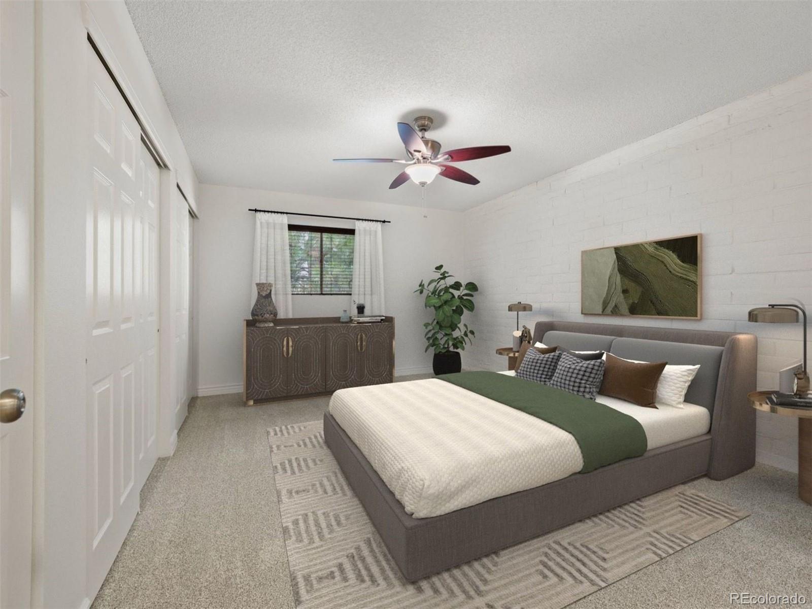 Staged bedroom with a gray upholstered bed, green runner, white brick wall, and ceiling fan.