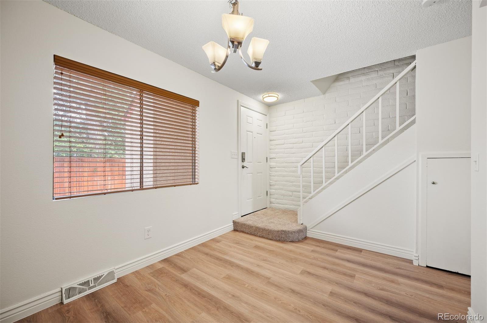 Vacant condo entryway with wood flooring, a white brick wall, and stairs beside a large window.