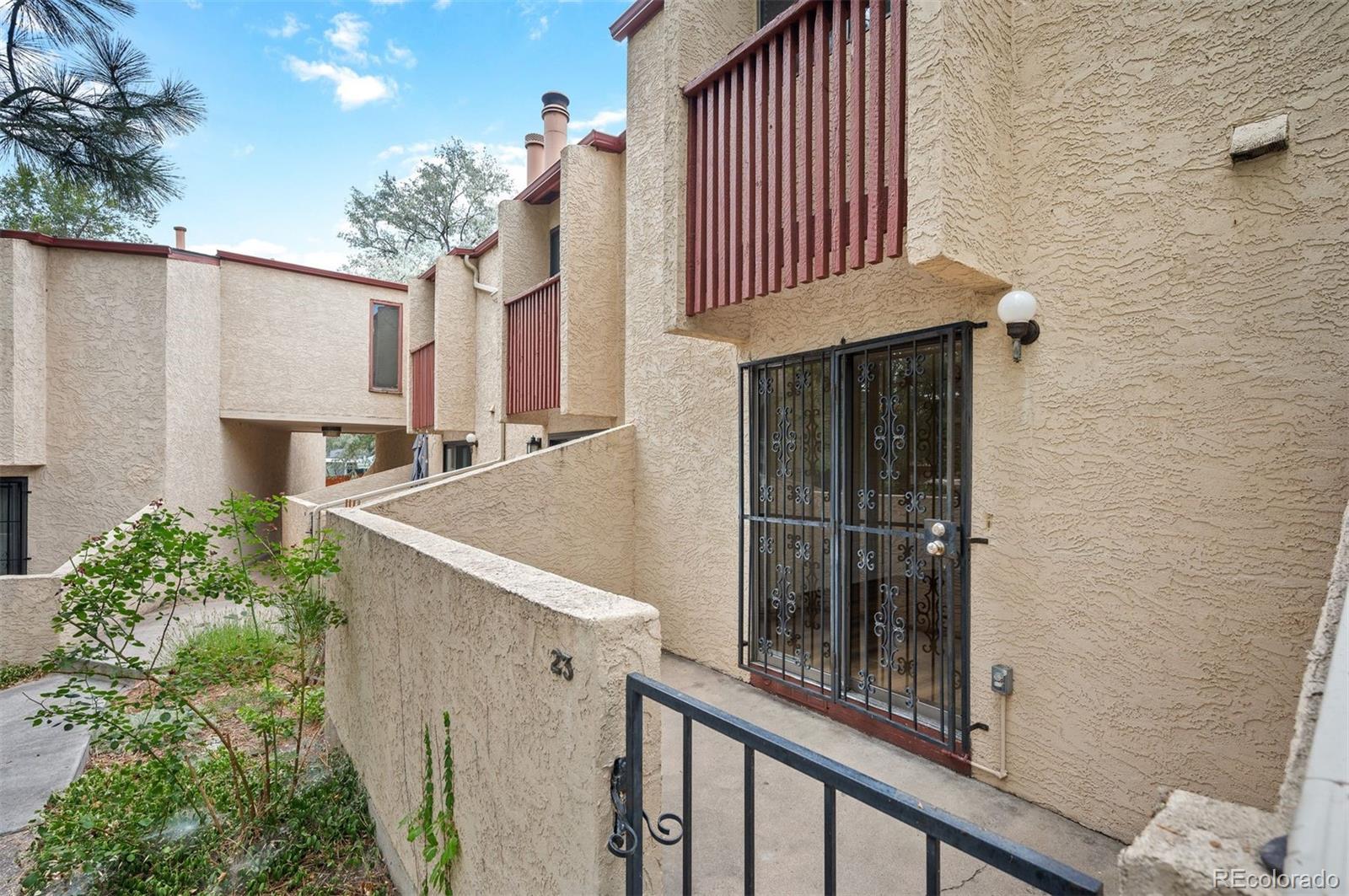 Condominium entrance with a black security gate, stucco walls, and red-brown balcony railings.