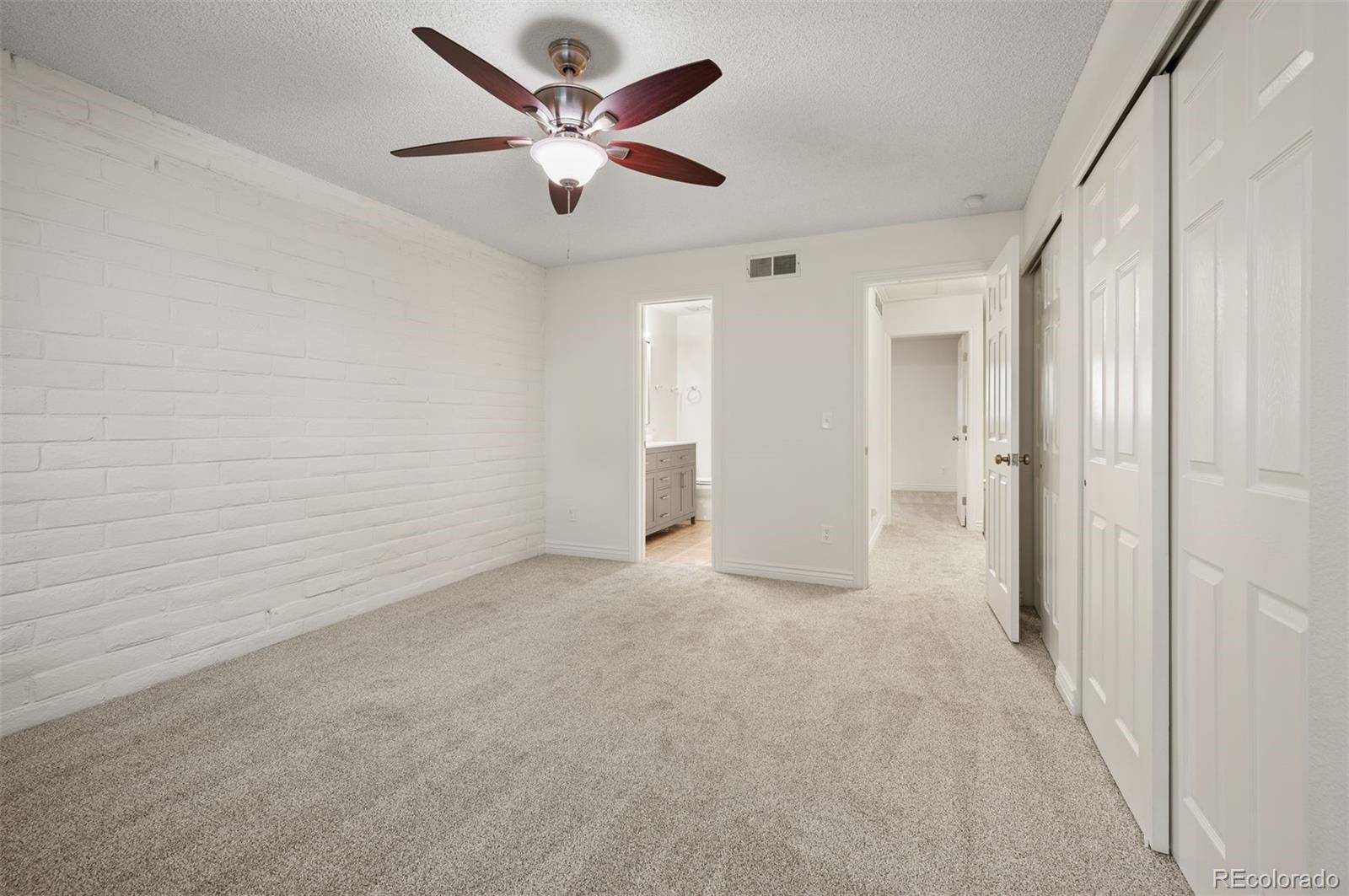Empty bedroom with carpet, a white brick accent wall, and a ceiling fan.