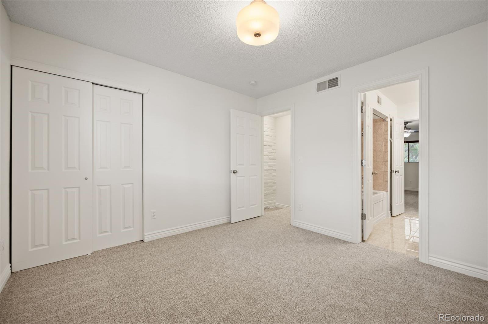 Empty bedroom with beige carpet, a double-door closet, and open bathroom doorway.