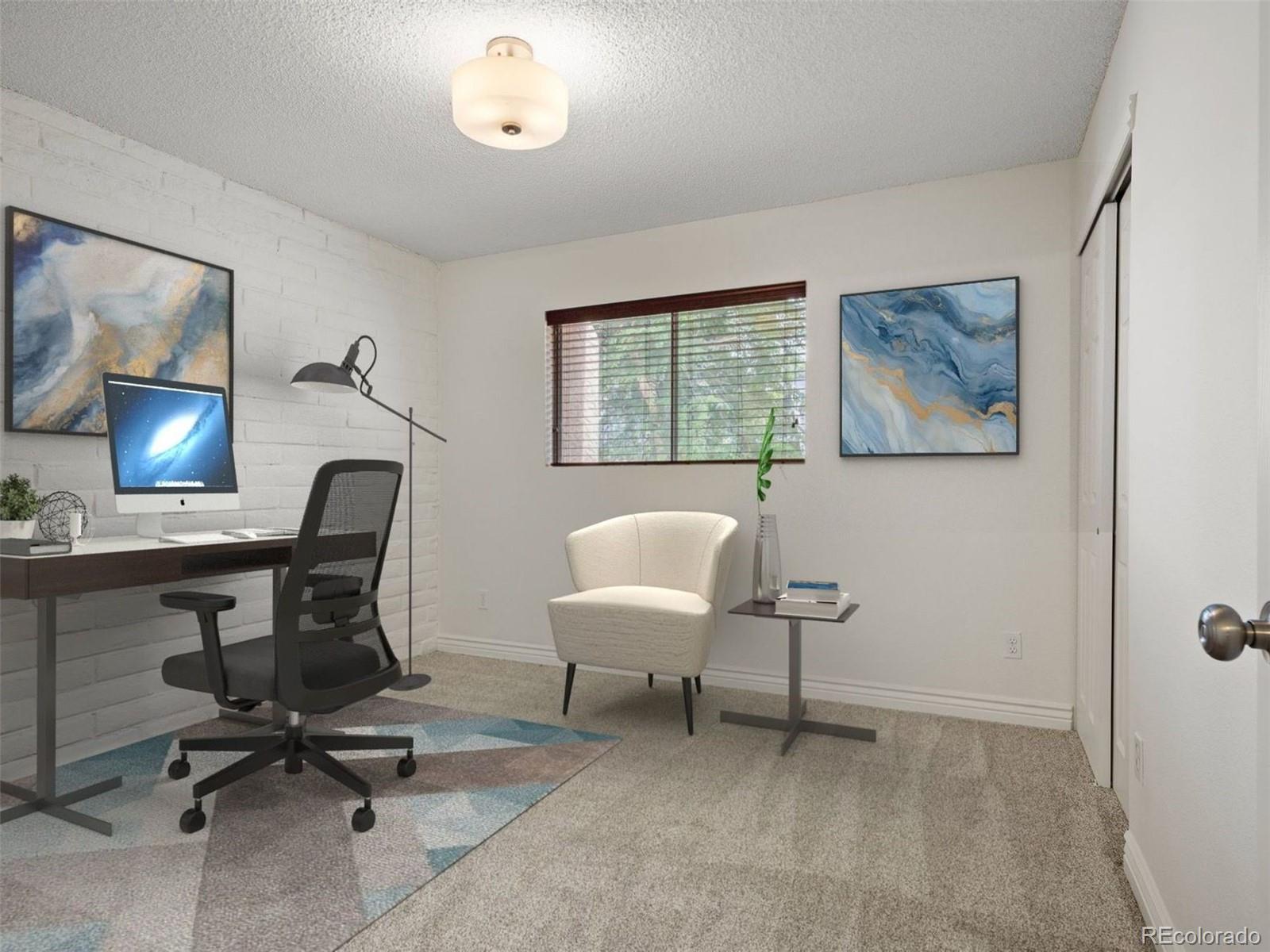 Staged home office with a desk and computer beside a white armchair and window.