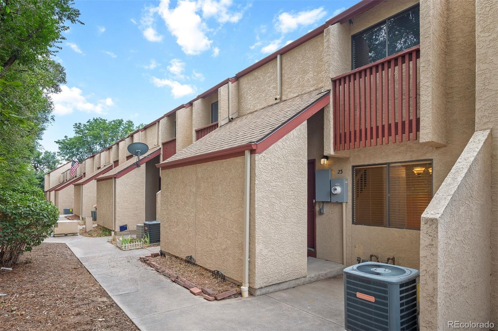 Condominium exterior with unit 23 entrance, red balcony railing, and an air-conditioning condenser.