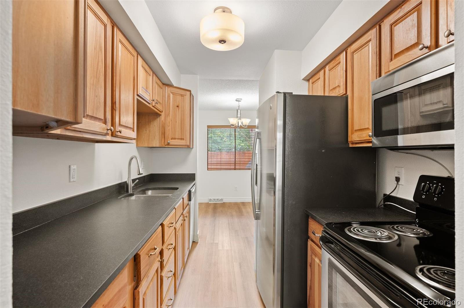 Galley kitchen with wood cabinets, dark countertops, stainless steel refrigerator, and electric range.