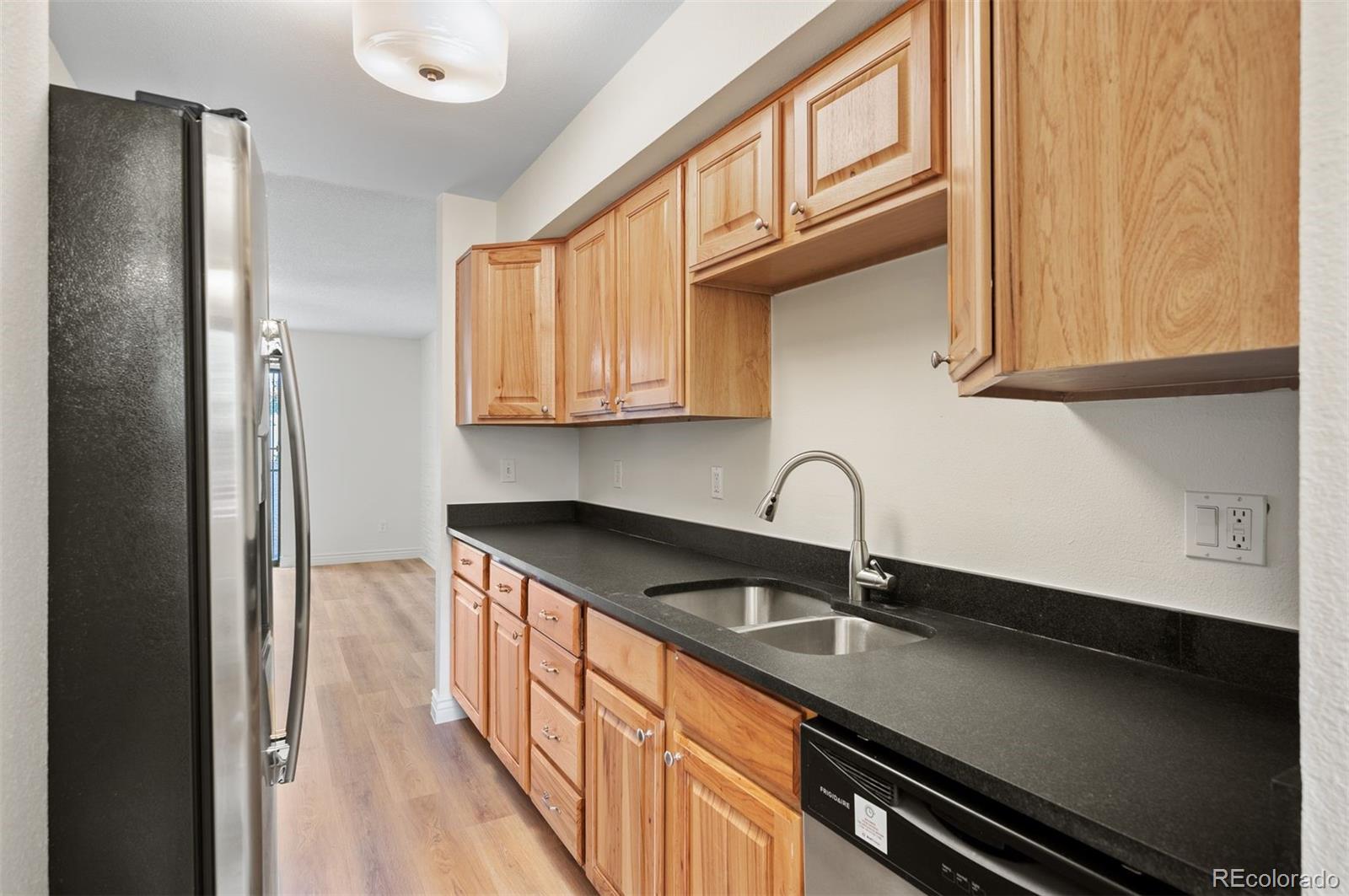 Kitchen with honey-colored cabinets, dark countertops, a double-basin sink, and stainless steel appliances.