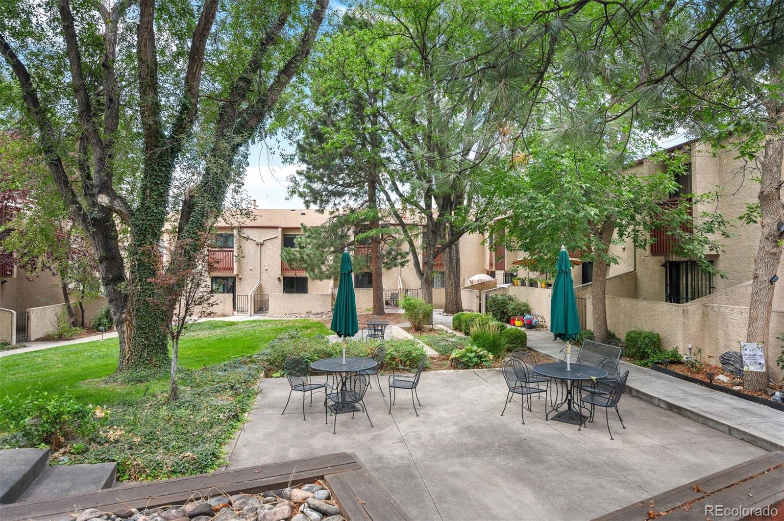 Condominium courtyard with mature trees, lawn, patio seating, and green umbrellas.