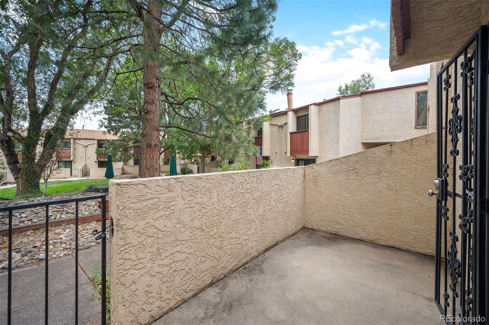 Ground-level condo patio with stucco walls and an iron gate overlooking a landscaped courtyard.