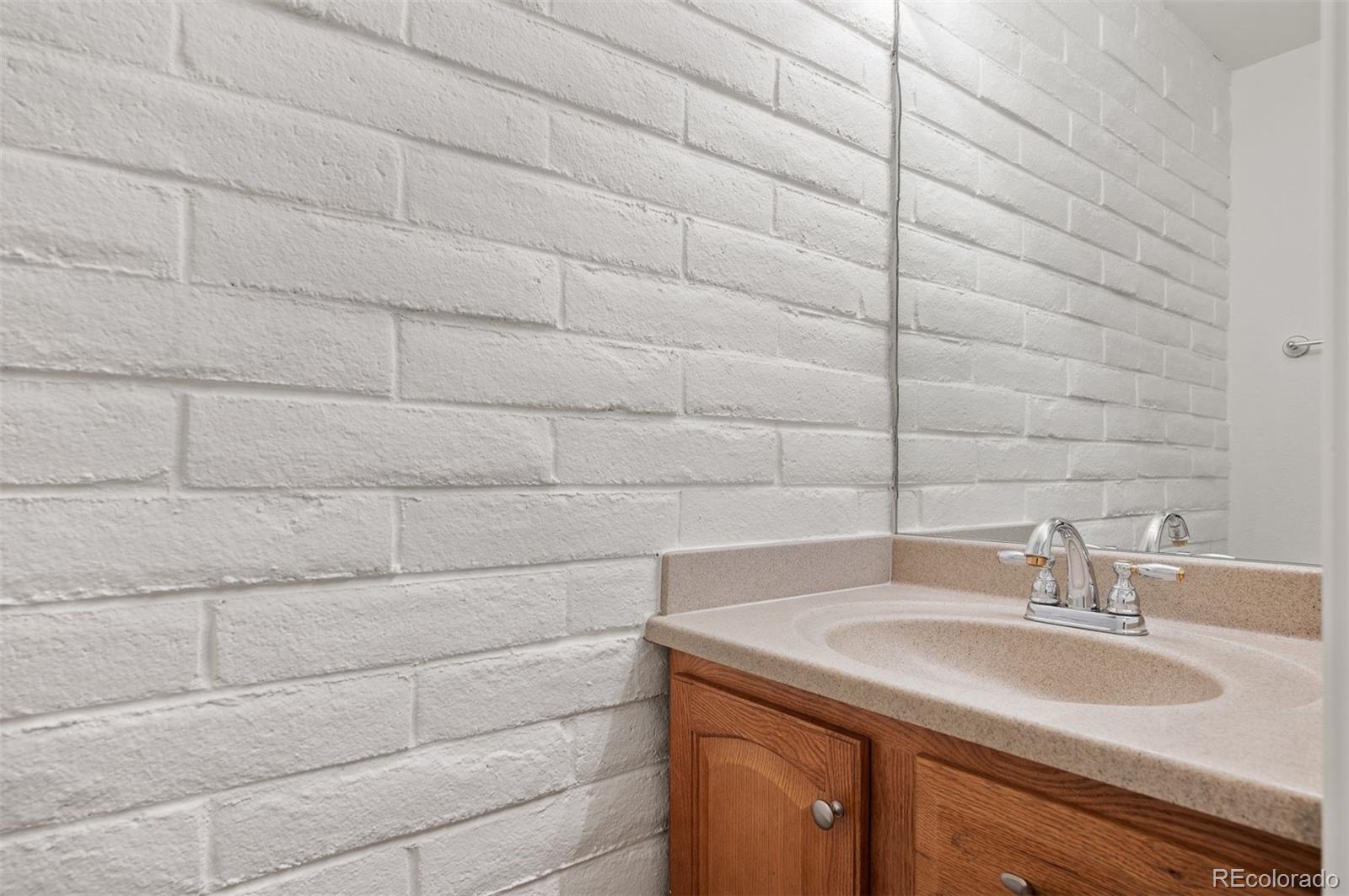 Bathroom vanity with an oak cabinet and beige sink against a white painted brick wall.