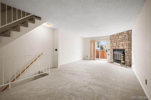 Empty living room with a stone fireplace, carpeted floor, staircase, and sliding glass doors to a patio.
