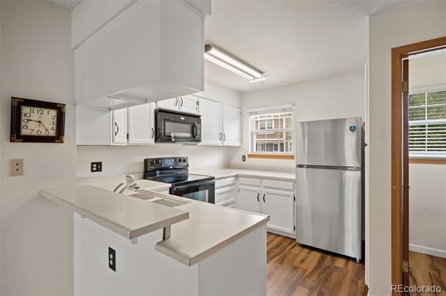 Kitchen with white cabinets, stainless steel appliances, peninsula counter, and wood-look flooring.