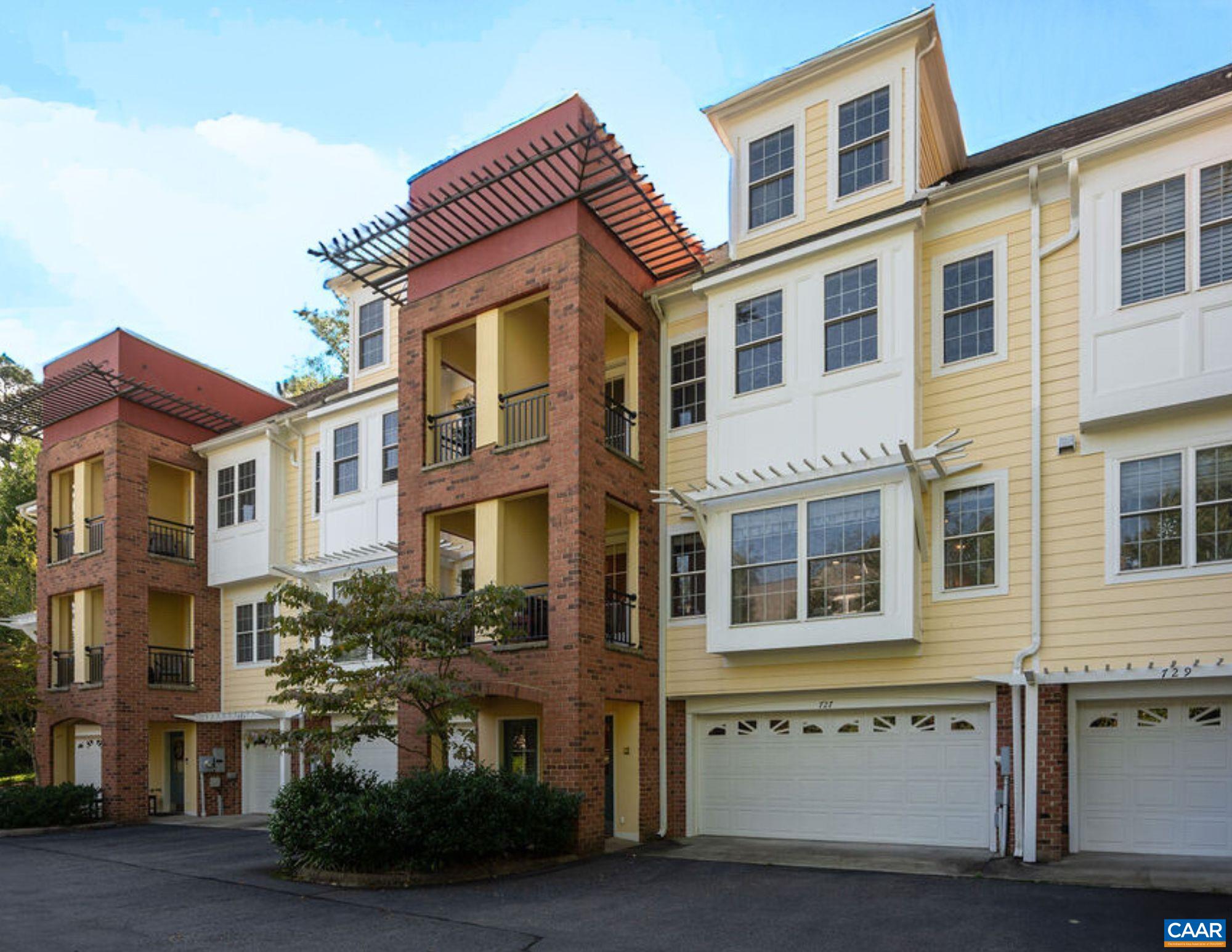 Attached yellow townhomes with red brick balconies, white-trimmed windows, and garages.