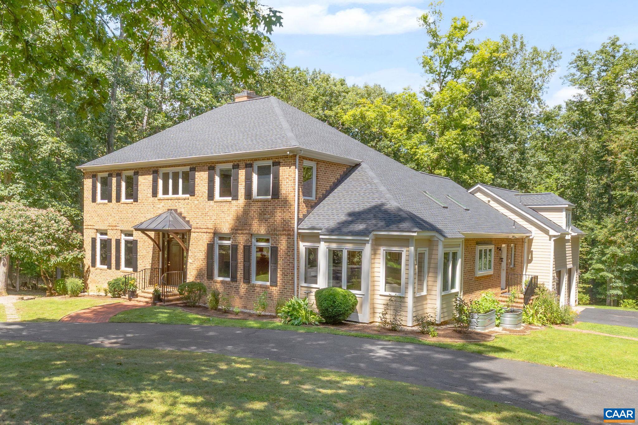 Two-story brick-and-siding house with a broad hipped roof, landscaped yard, and wooded surroundings.