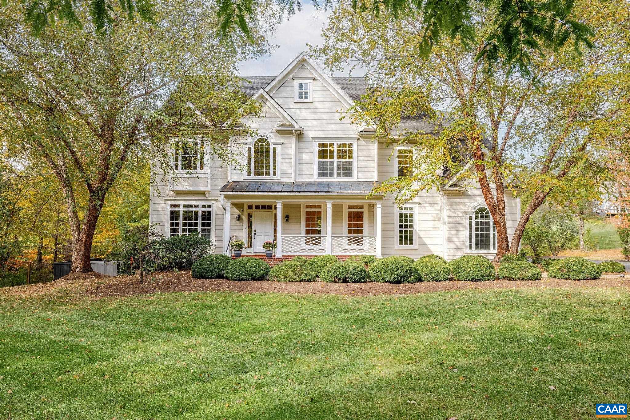 White two-story house with a covered porch, lawn, and autumn trees.
