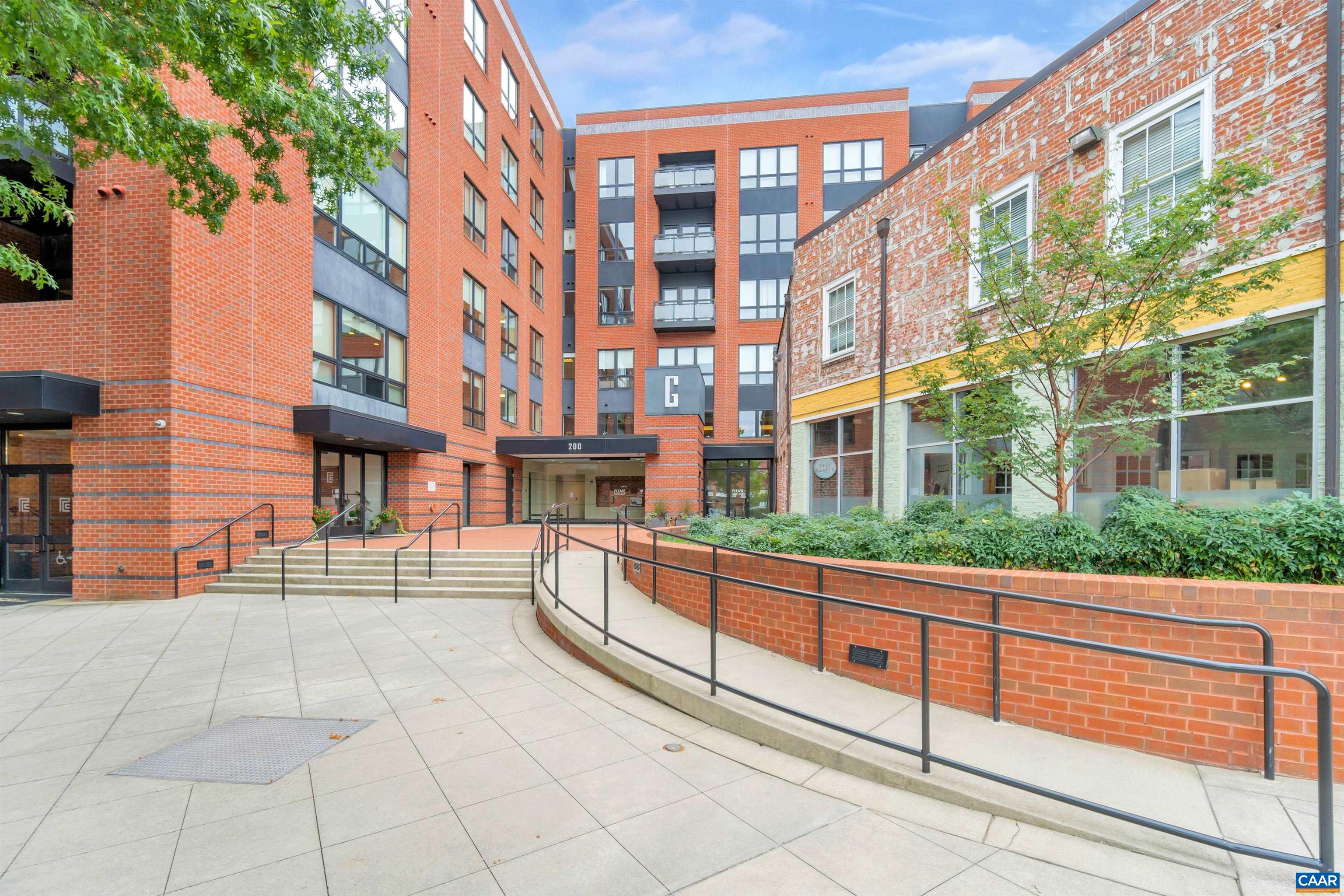 Red-brick building entrance with broad steps, an accessible ramp, and a planted courtyard.