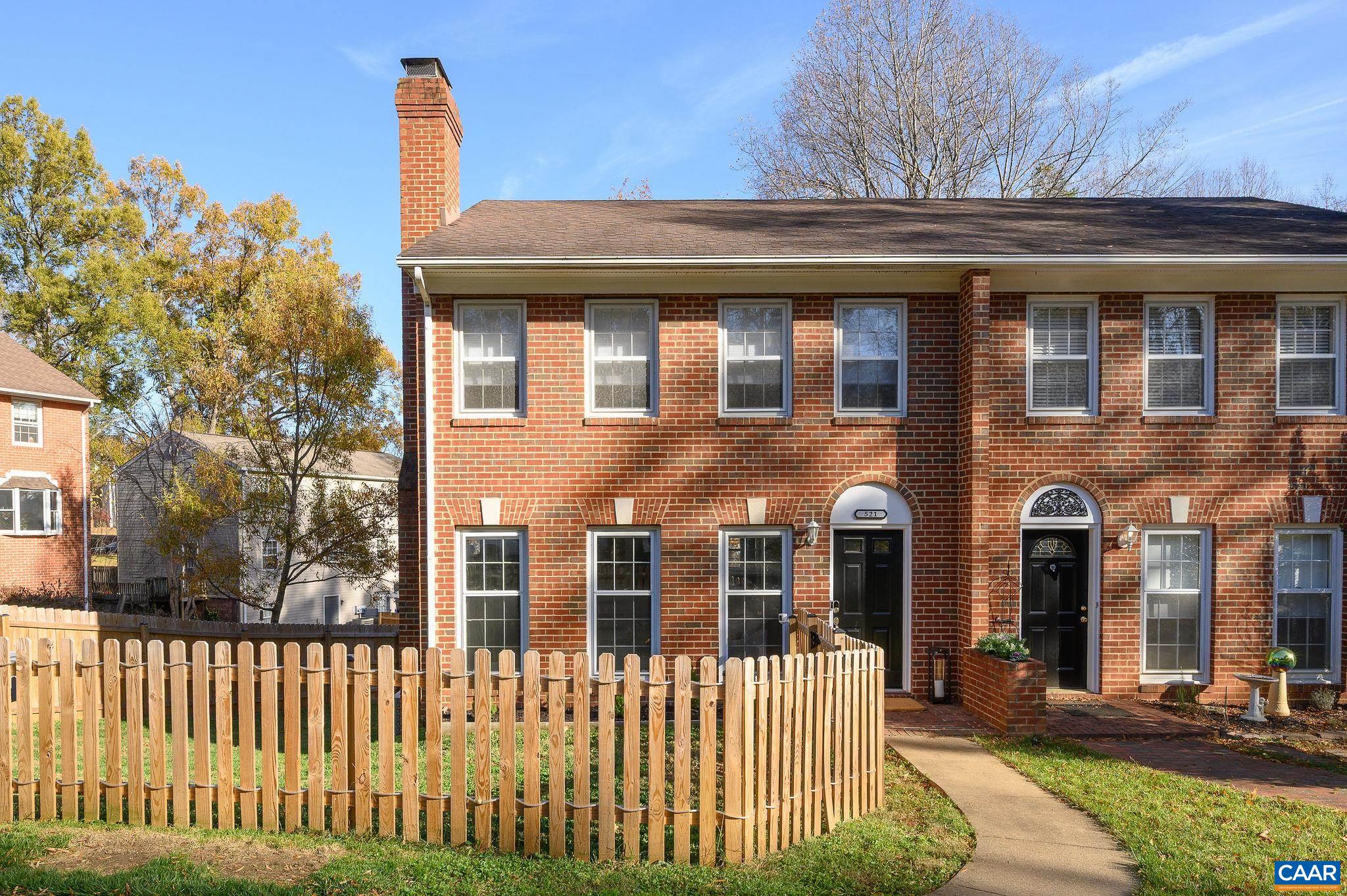 Red-brick townhomes with arched black doors and a fenced front yard.