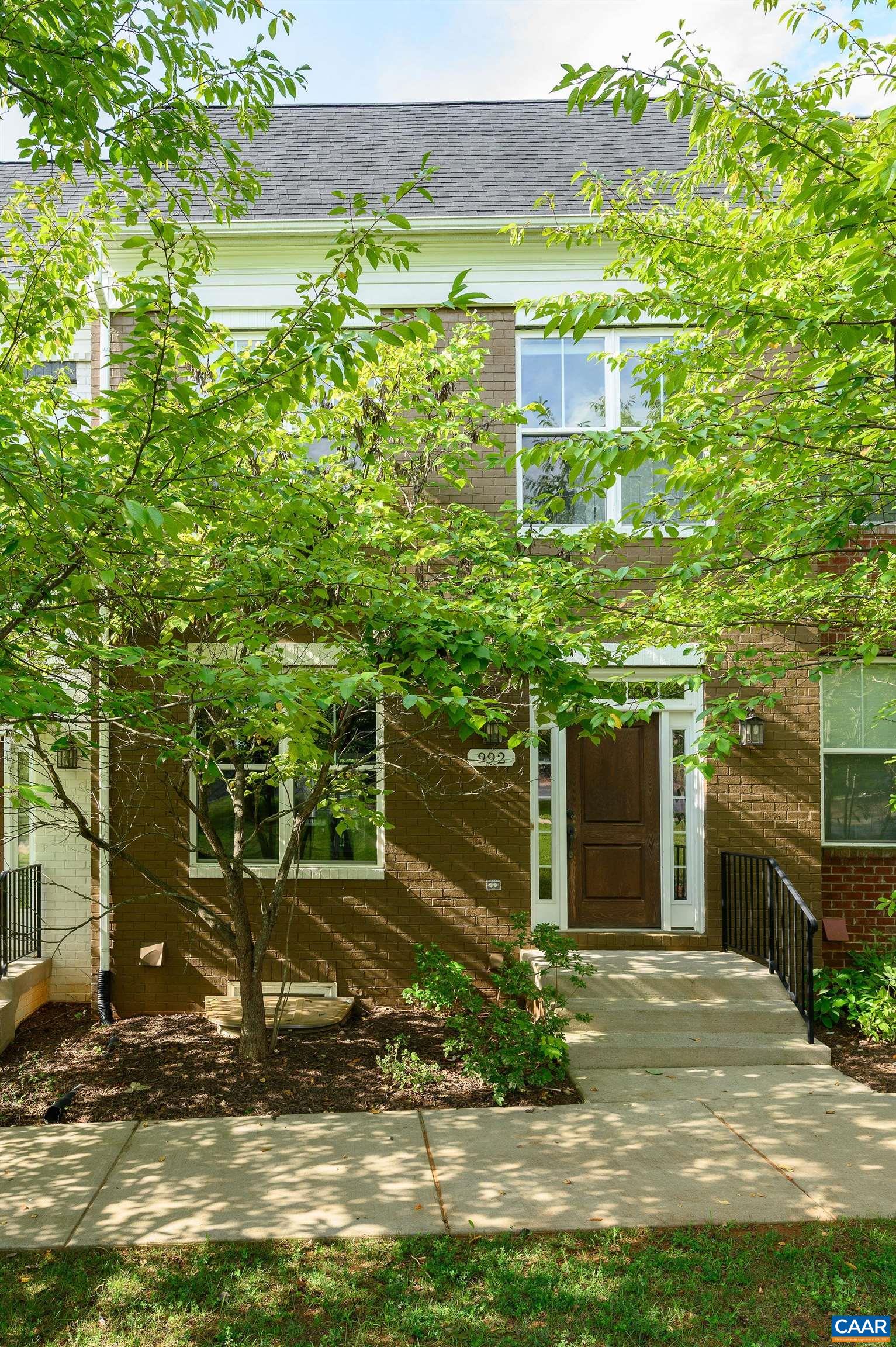 Brick home entrance with brown door and leafy trees framing the walkway.