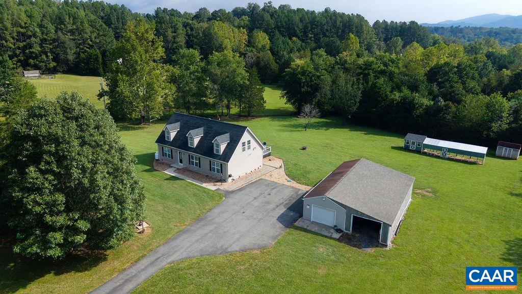 Aerial view of a two-story home and detached garage surrounded by a broad lawn and mature trees.