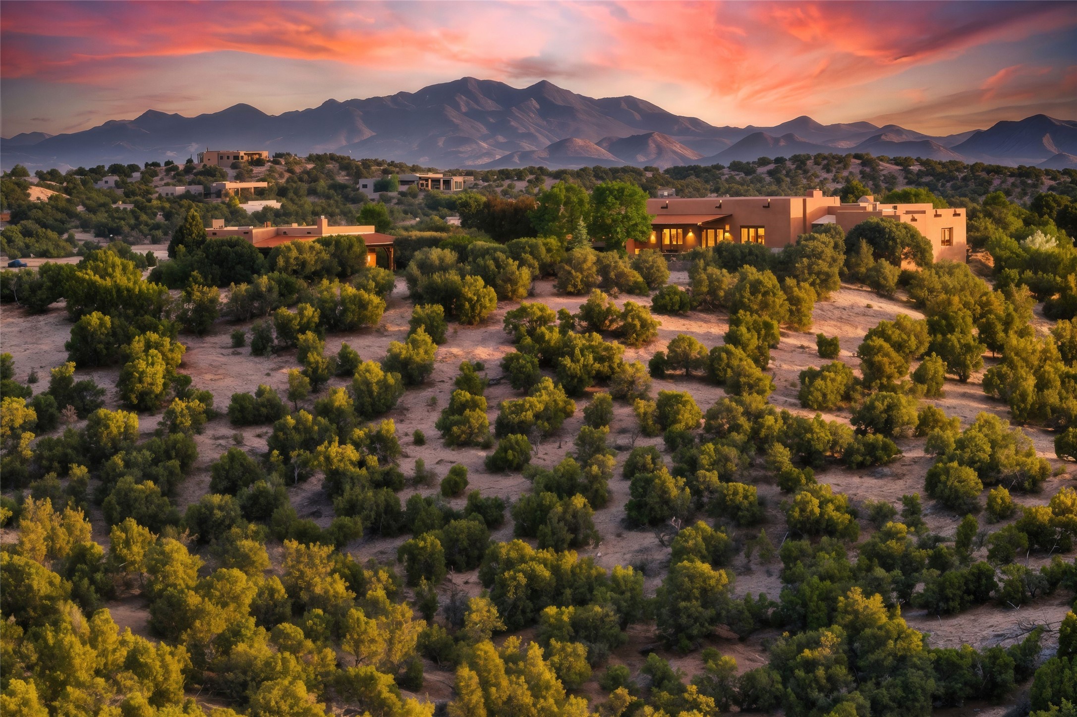 Adobe homes among desert scrub, with mountains in the background at sunset.