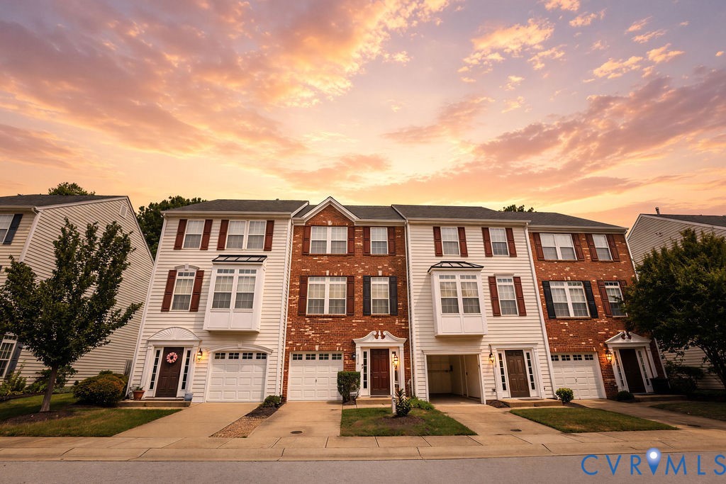 Attached brick and siding townhomes with garages beneath a colorful sunset sky.